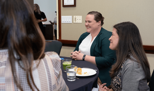Group of women sitting at a table talking business and smiling.