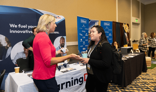 Two women standing in front of the eLearningDOC booth at the TSAE conference, talking.