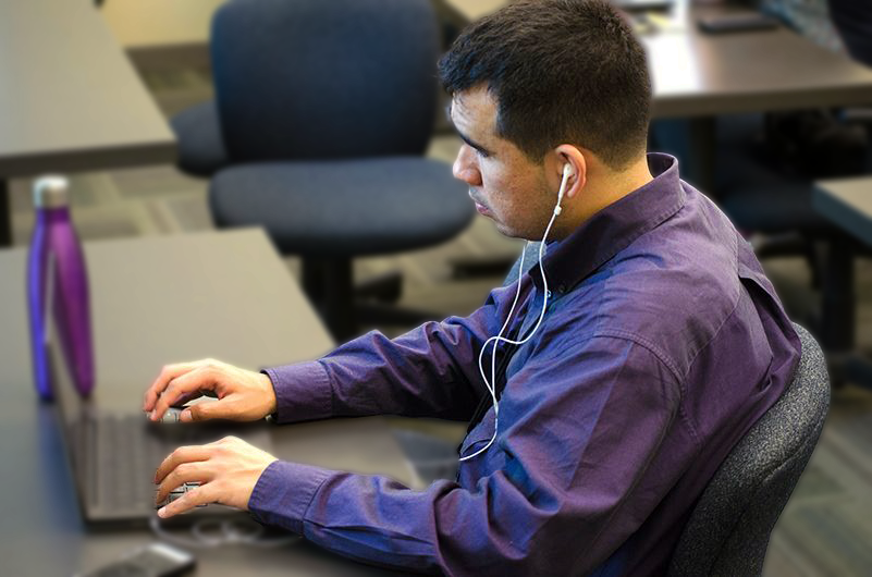 Man wearing headphones and working on laptop at desk.