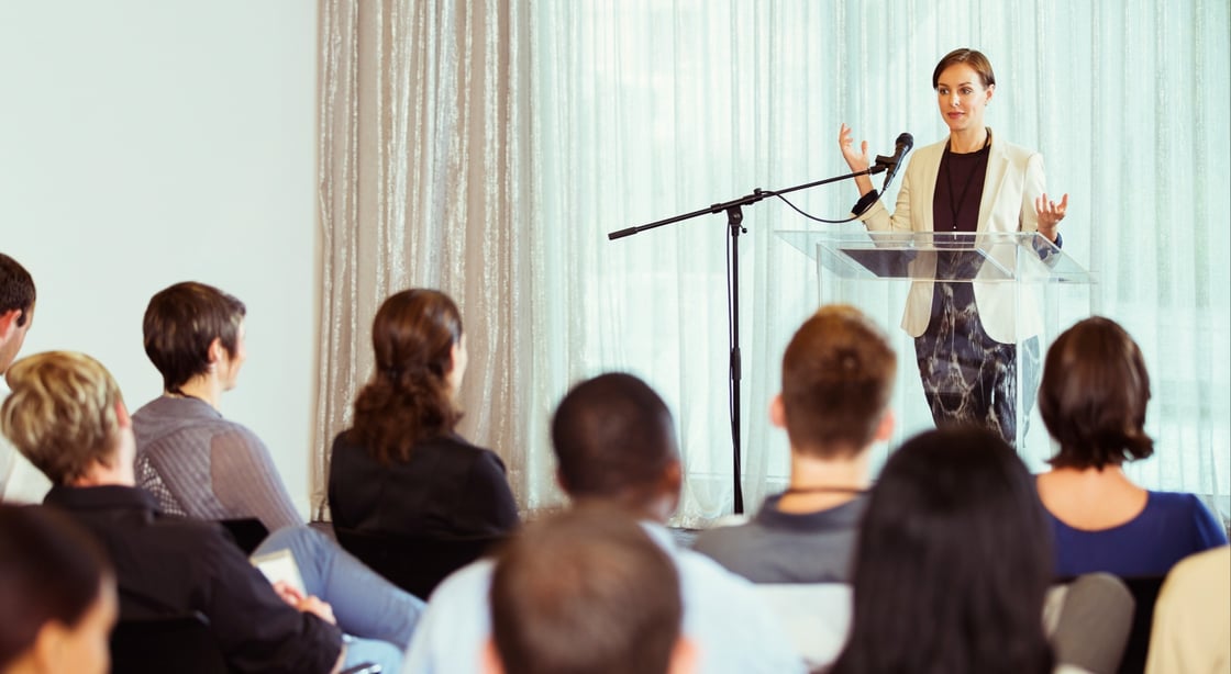 Woman presenting to group at a conference.